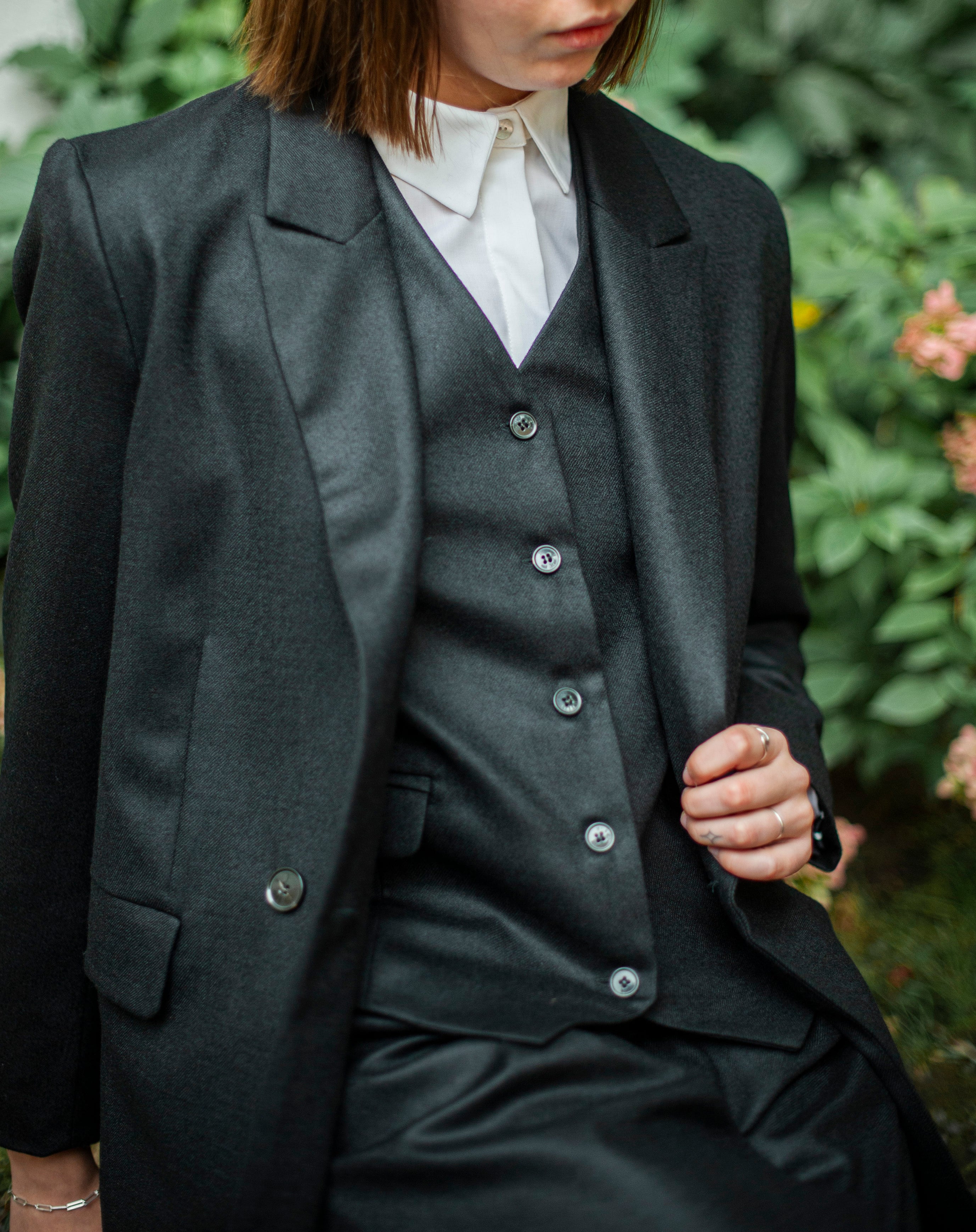 Black wool waistcoat with a button closure layered over a white dress shirt.   Black classic suit vest for women.
