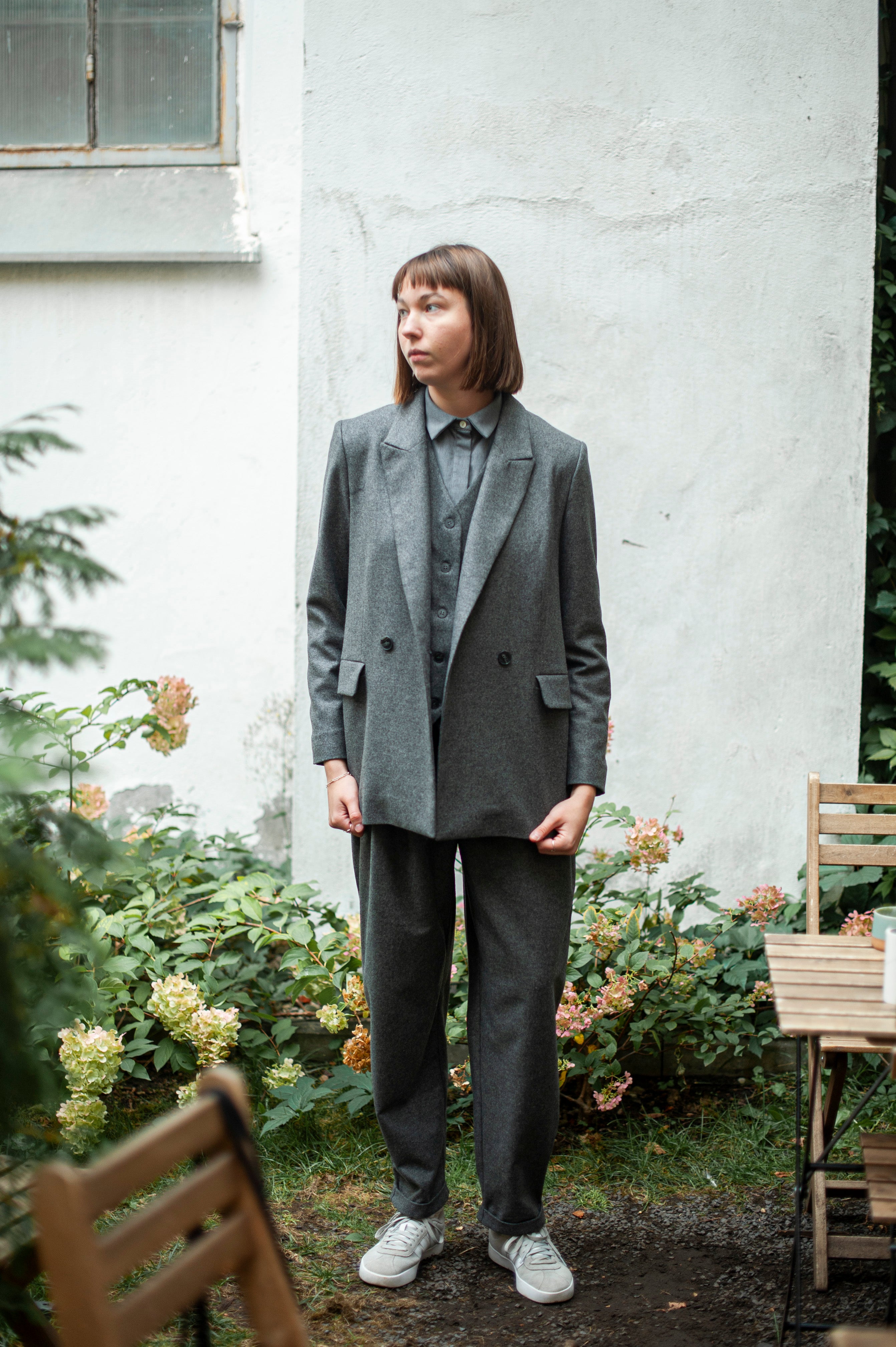 Grey wool jacket paired with tapered leg pants made of tweed wool. The pants feature front pleats, a zipper closure, and classic belt loops. Your perfect timeless pants to match every  occasion.