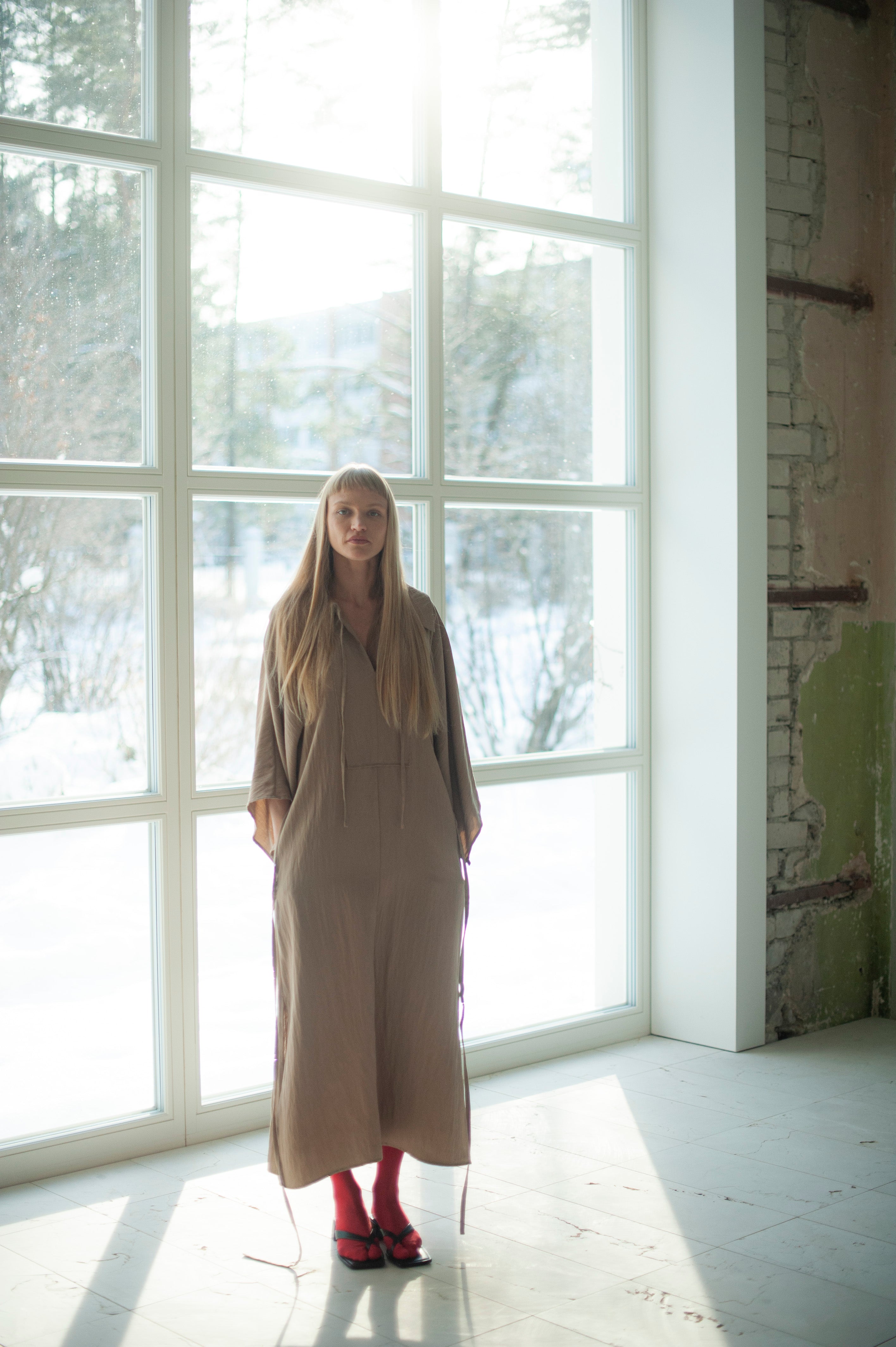 Sand beige dress made from the cupro fabric, also known as rayon. The dress features wide kimono-style inspired sleeves, a large shirt collar and side slits on sleeves and hem. There is also a long waist tie.