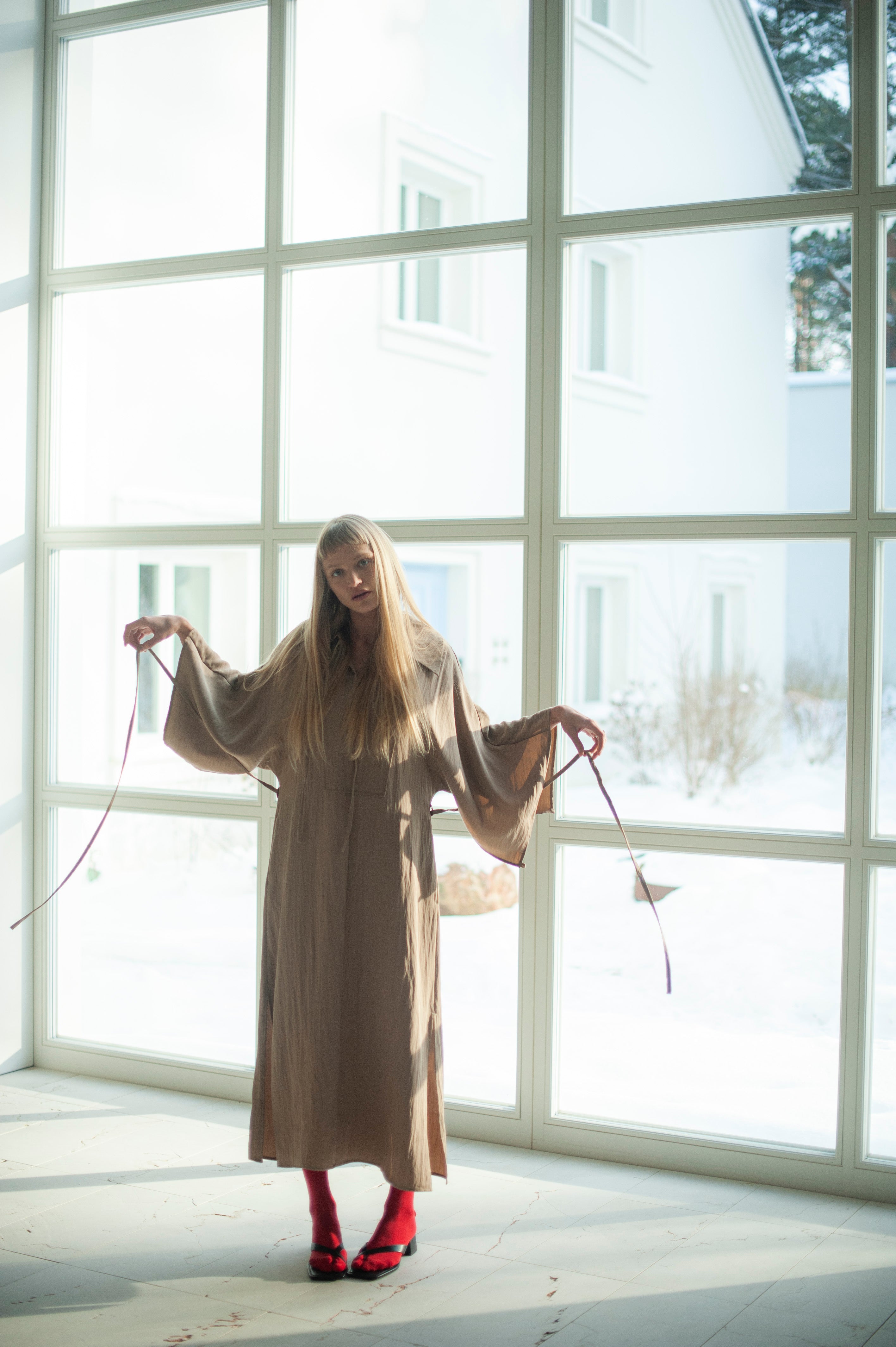 Sand beige dress made from the cupro fabric, also known as rayon. The dress features wide kimono-style inspired sleeves, a large shirt collar and side slits on sleeves and hem. There is also a long waist tie.