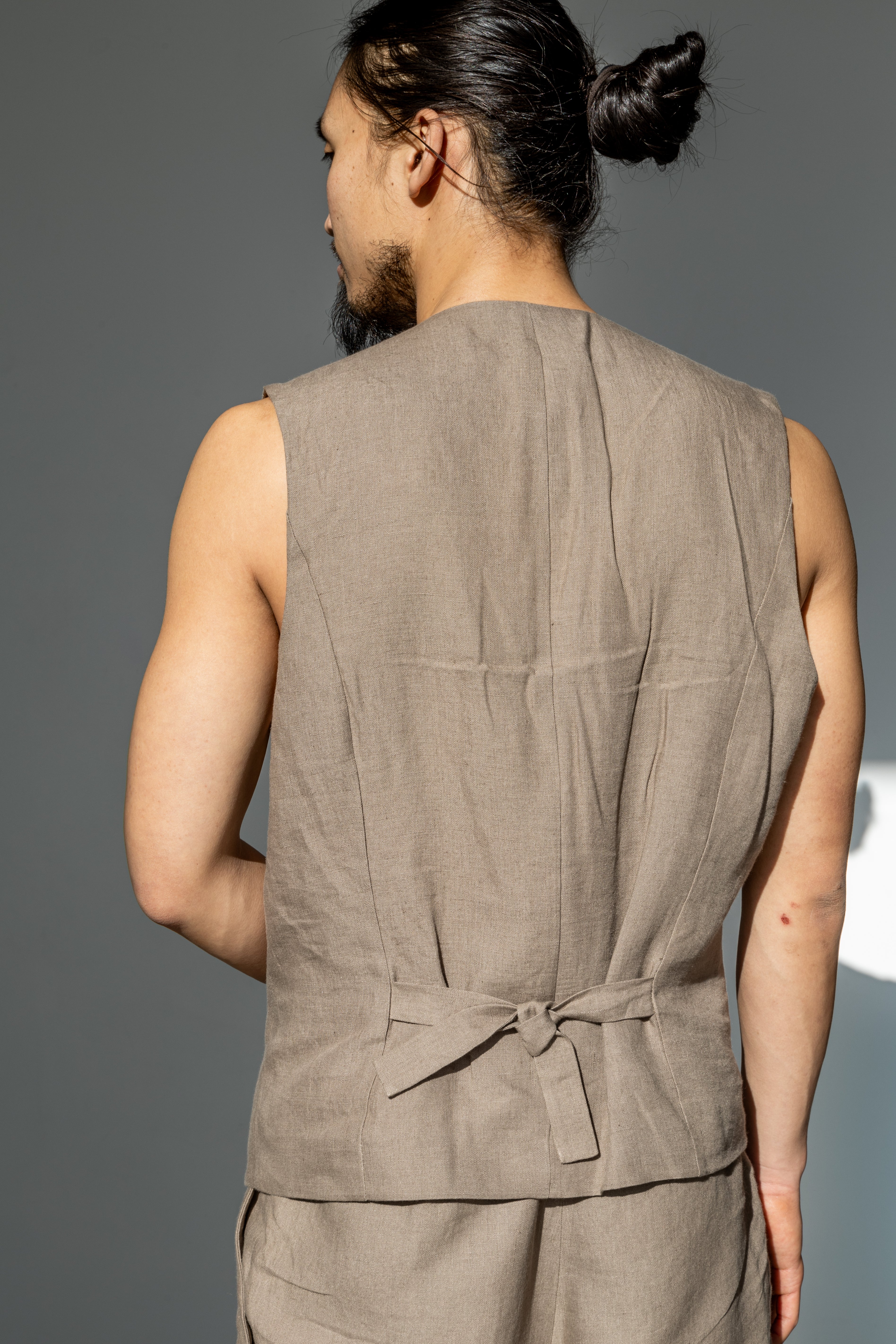 A cinched back of a beige linen suit waistcoat. Adjustable back on a beige linen vest.