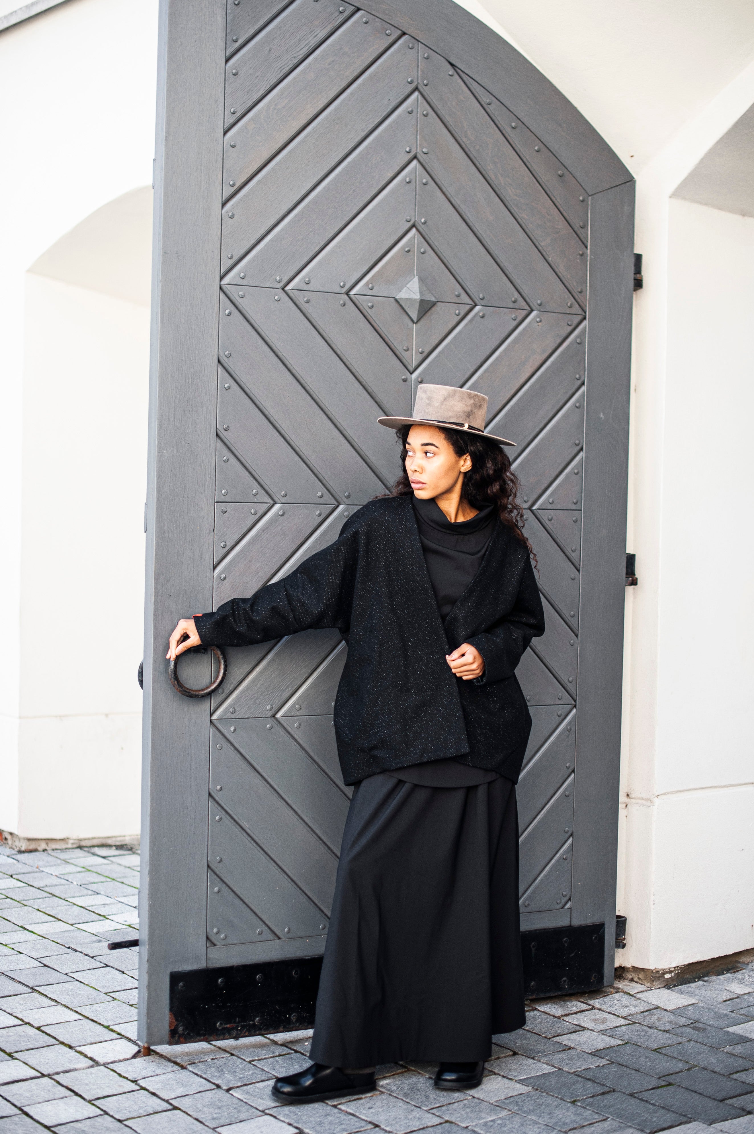 An outfit of a black blouse, a black jacket, and a black A-line skirt with an elasticated waistband.