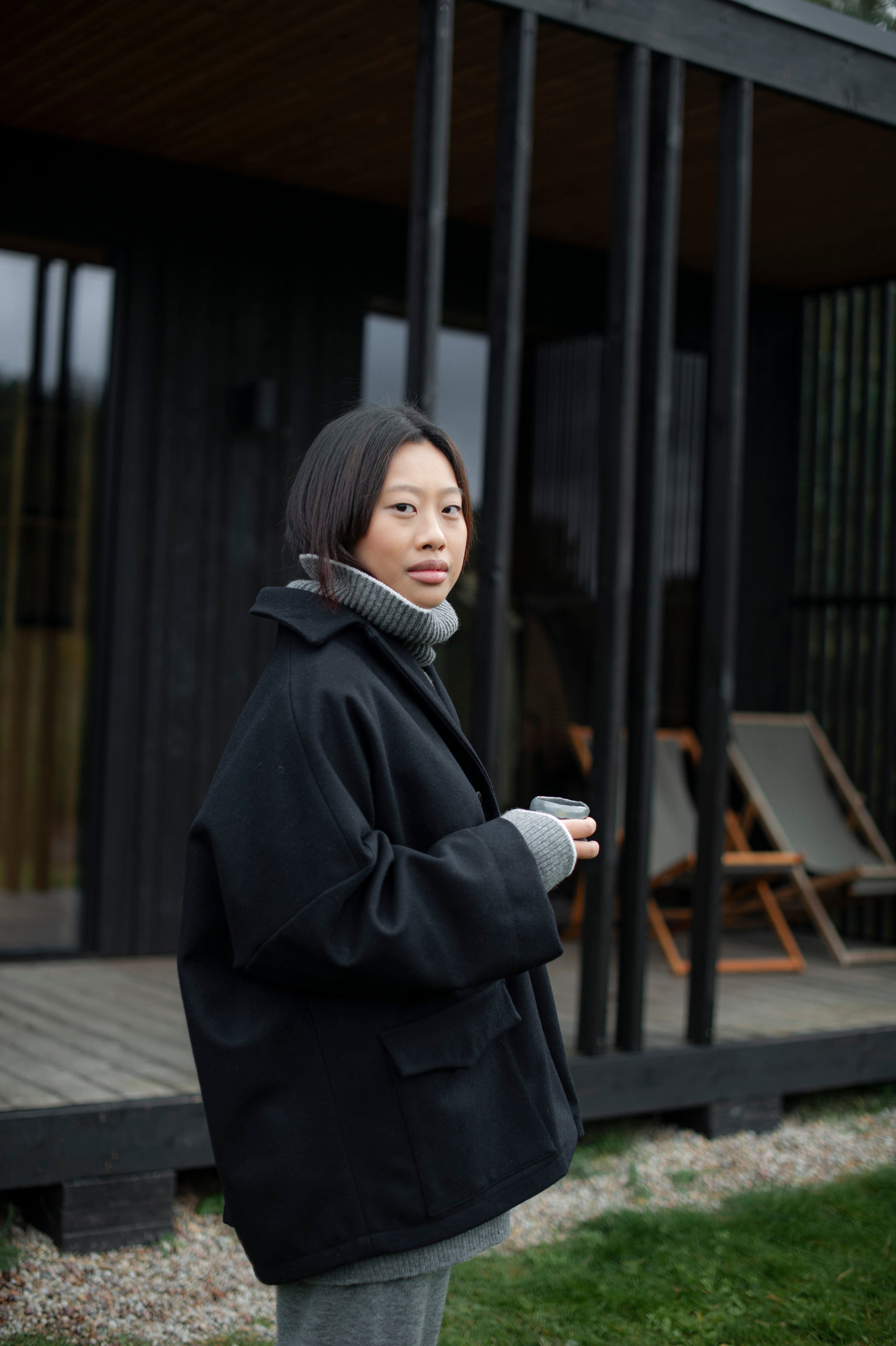 Women's dense boiled wool jacket in a boxy oversized silhouette. The jacket comes in one size only and is pictured paired with a grey knit set of a high-neck jumper and wide pants.