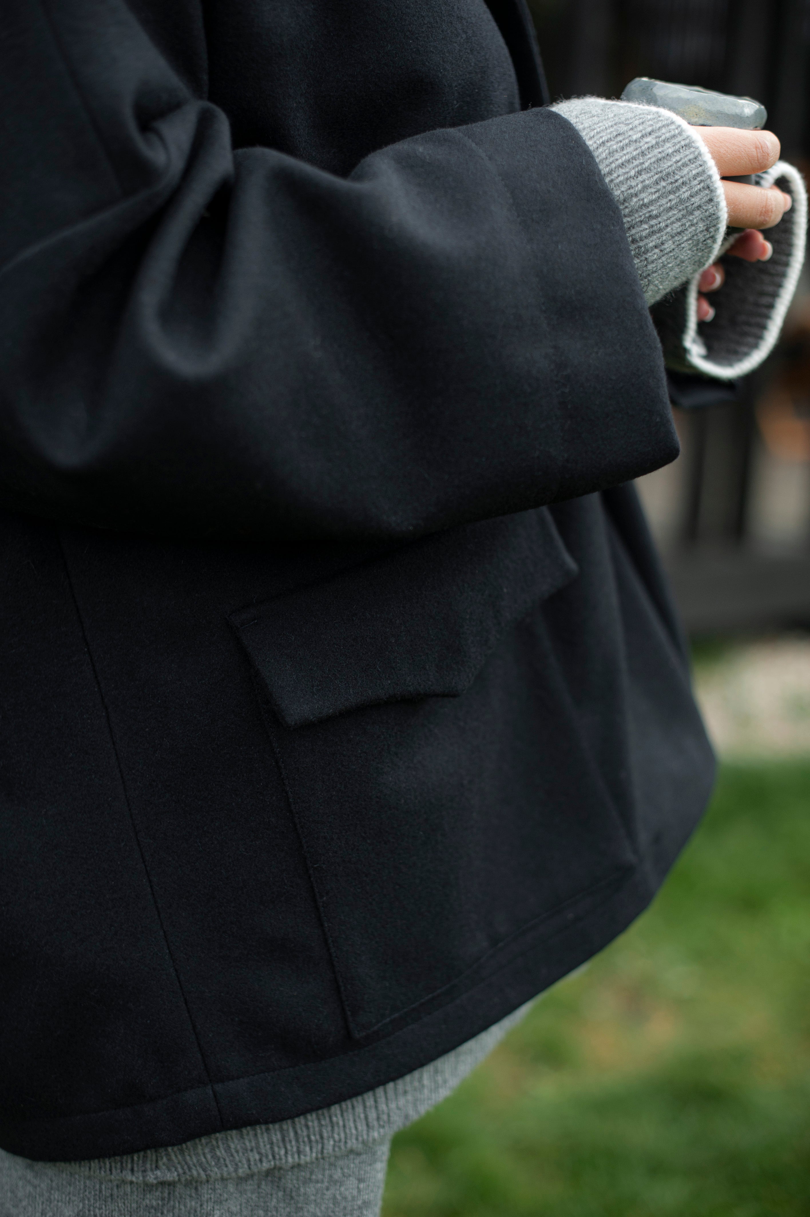 Women's dense boiled wool jacket in a boxy oversized silhouette. The jacket comes in one size only and is pictured paired with a grey knit set of a high-neck jumper and wide pants.