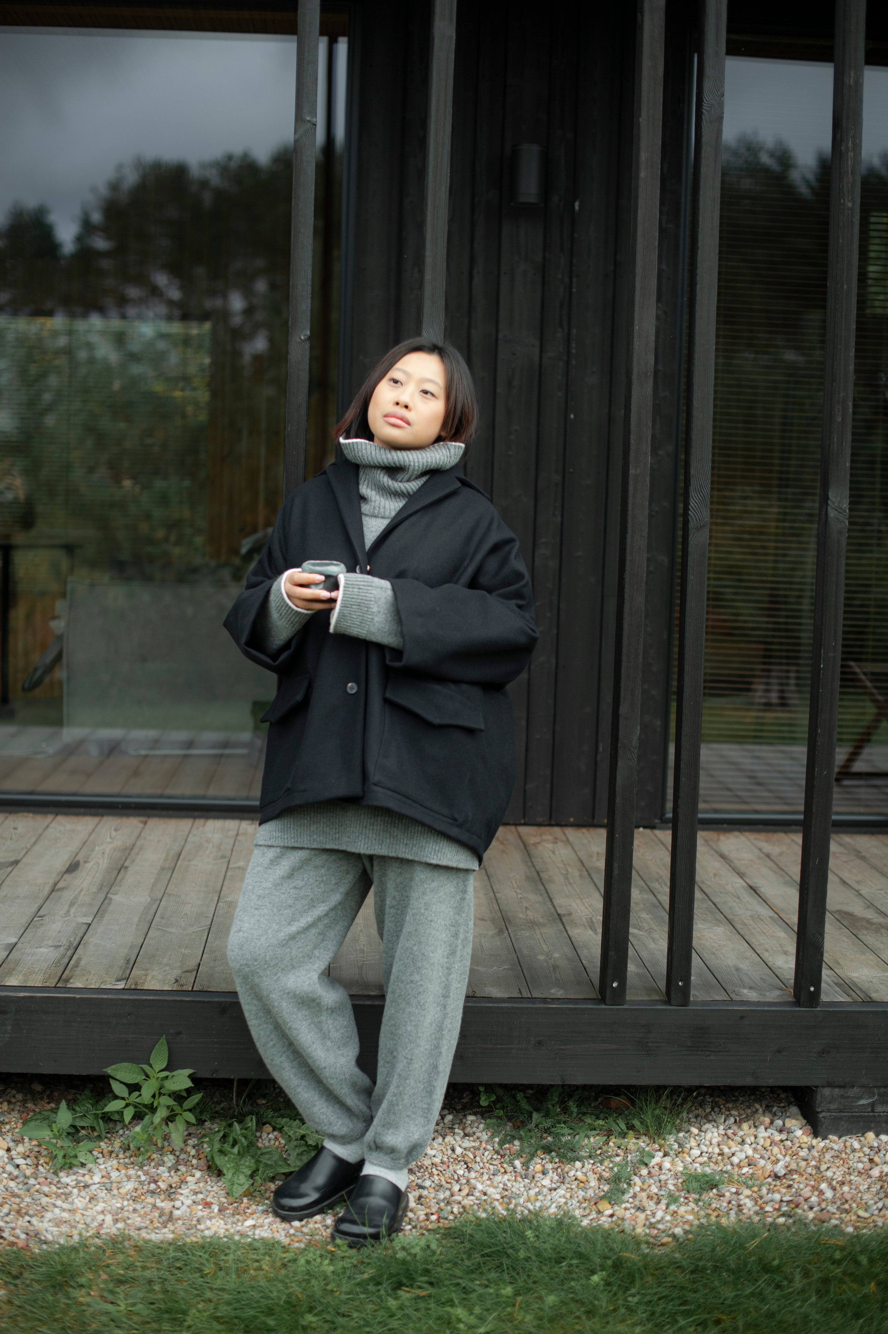 Women's dense boiled wool jacket in a boxy oversized silhouette. The jacket comes in one size only and is pictured paired with a grey knit set of a high-neck jumper and wide pants.