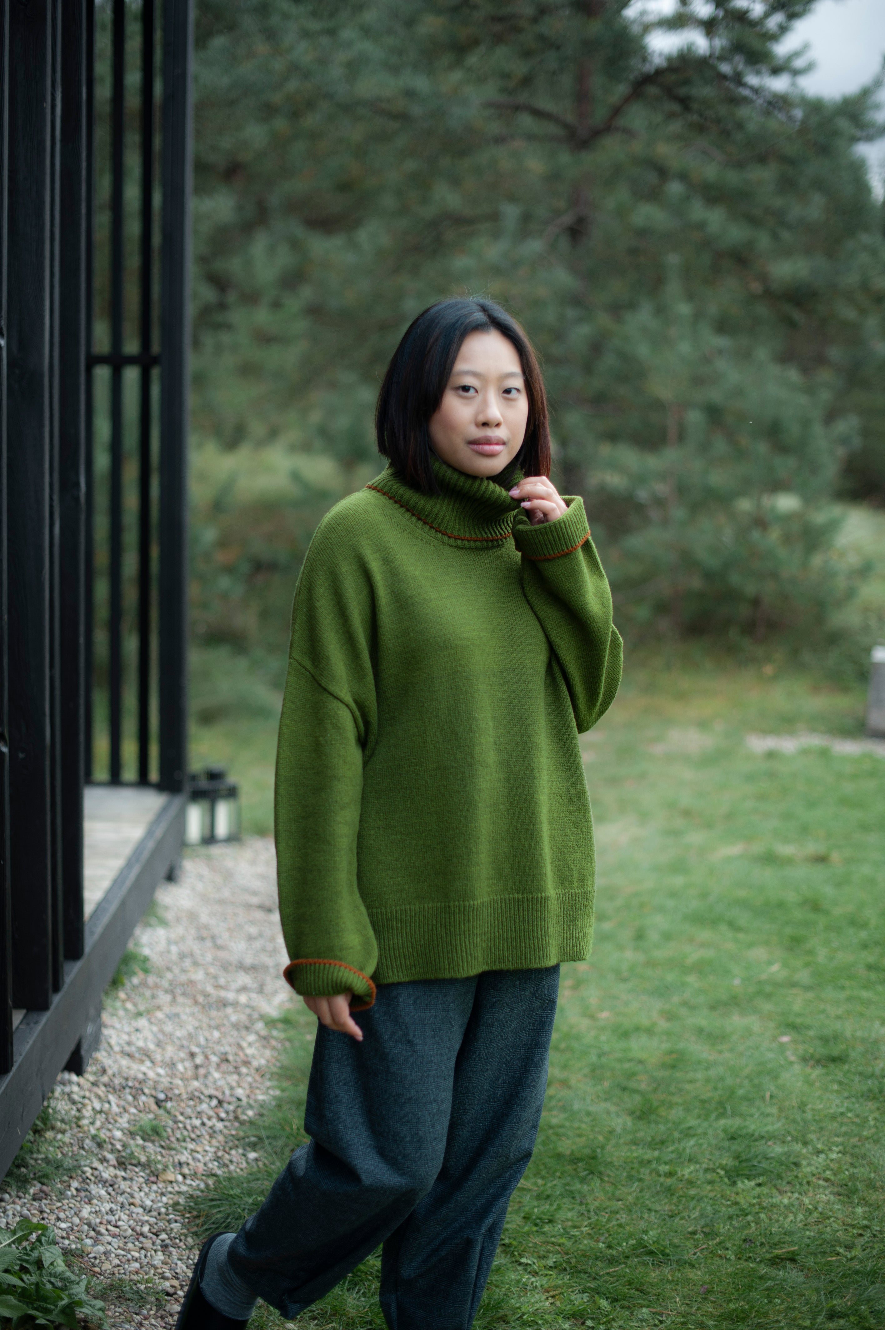 Green merino wool jumper boasting contrasting lines on the cuffs and high-neck, paired with brown pants