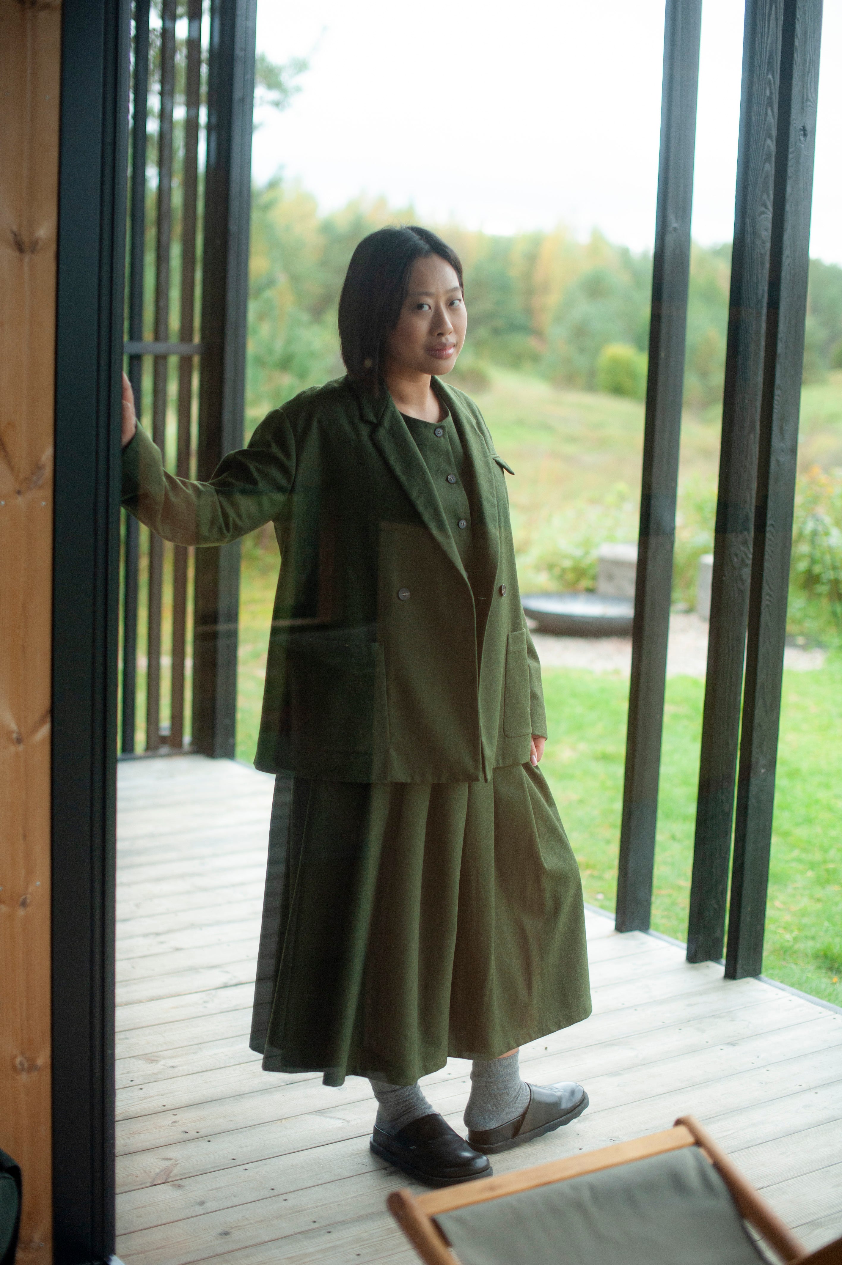 Boxy-fit green wool-blend blazer with a double-breasted closure, large patch pockets, and a decorative pocket square detail. The blazer is paired with coordinating culottes featuring a pleated waistband.