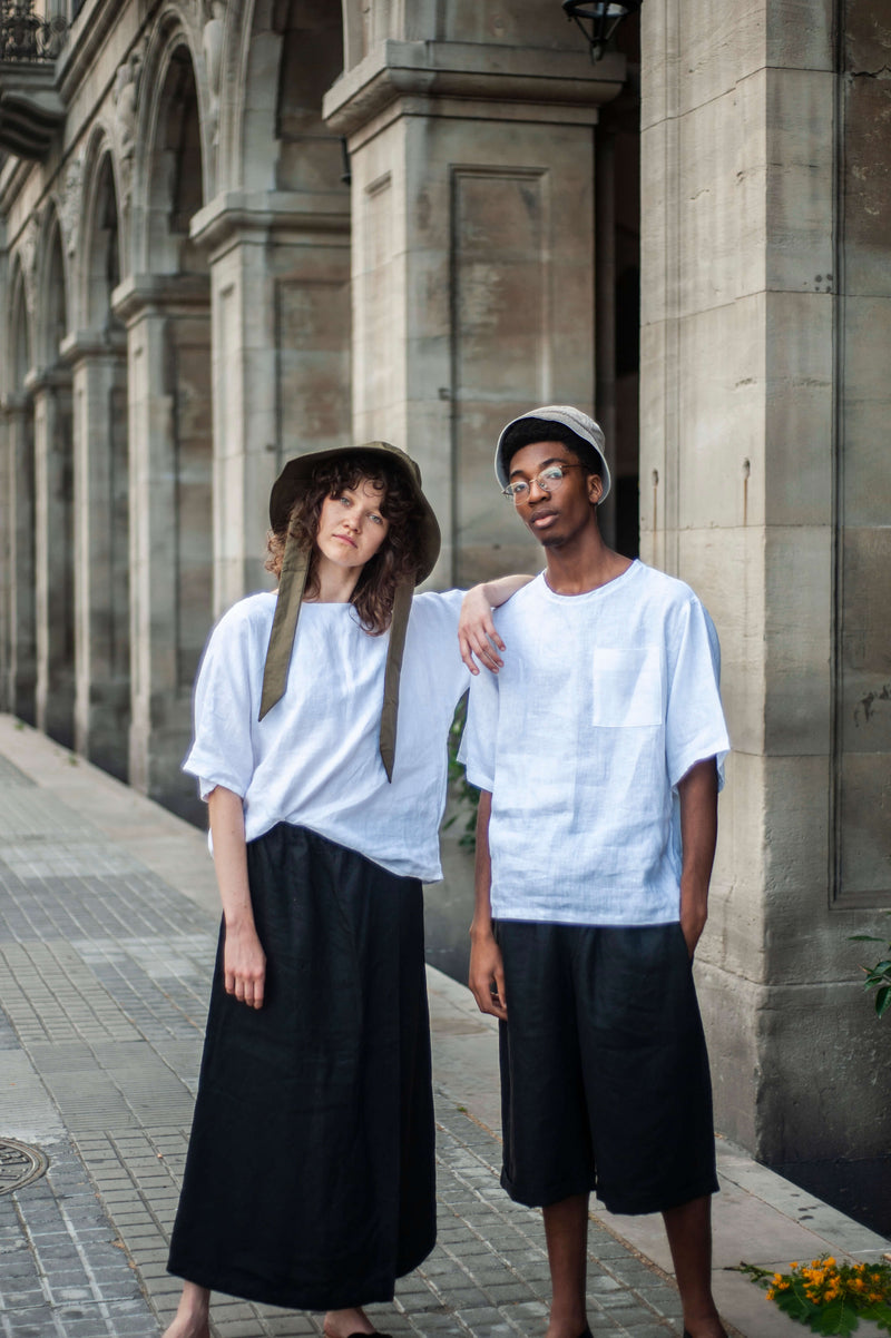 A girl wearing wide-leg linen pants and a man in loose-fit shorts. Both wearing white oversized linen shirts.