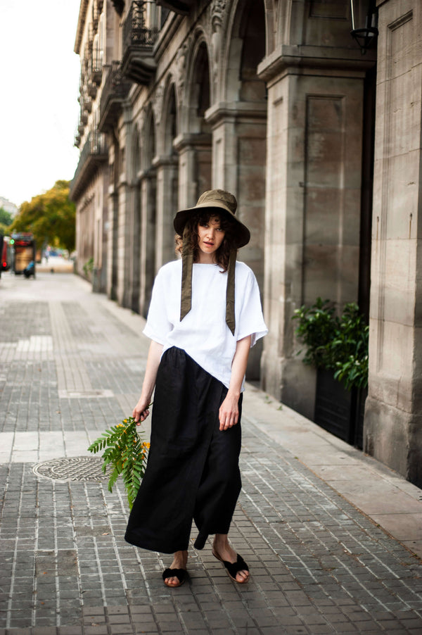 Minimalist and comfortable black linen palazzo pants with an elasticated waistband and side pockets. Paired with a white T-shirt and khaki hat.