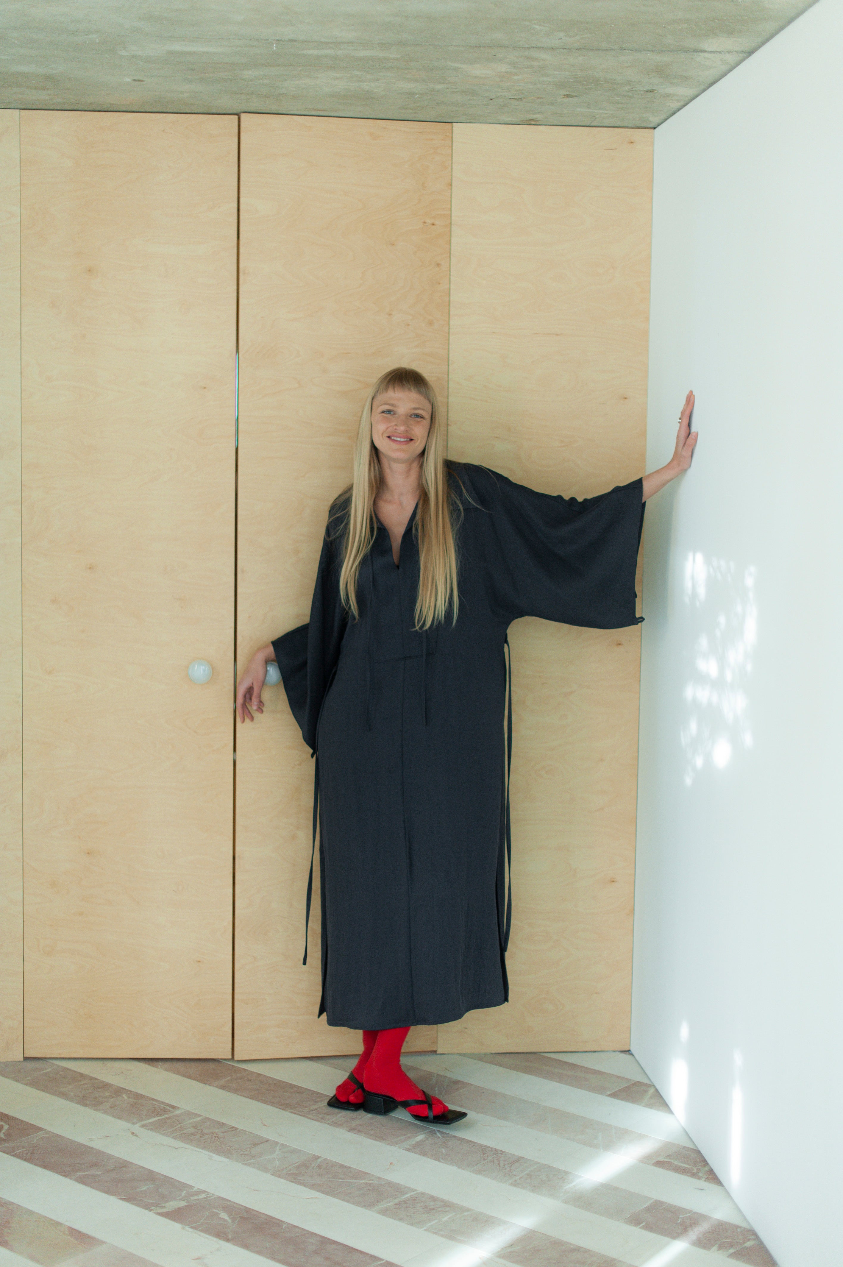A blonde woman in a long wide dress with kimono sleeves and a slim waist tie.