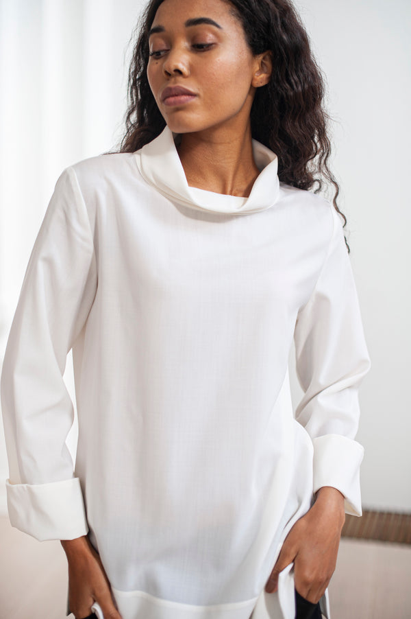 Women's white blouse featuring a high, relaxed neckline resembling a turtleneck. Wide hem and wide sleeve ends for an extra dose of comfort and elegance.