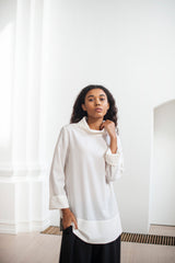 Long white blouse with side slits and a high neckline to elevate your casual style and give it some extra pinch of sophisticated. Paired with a black A-line silhouette skirt.