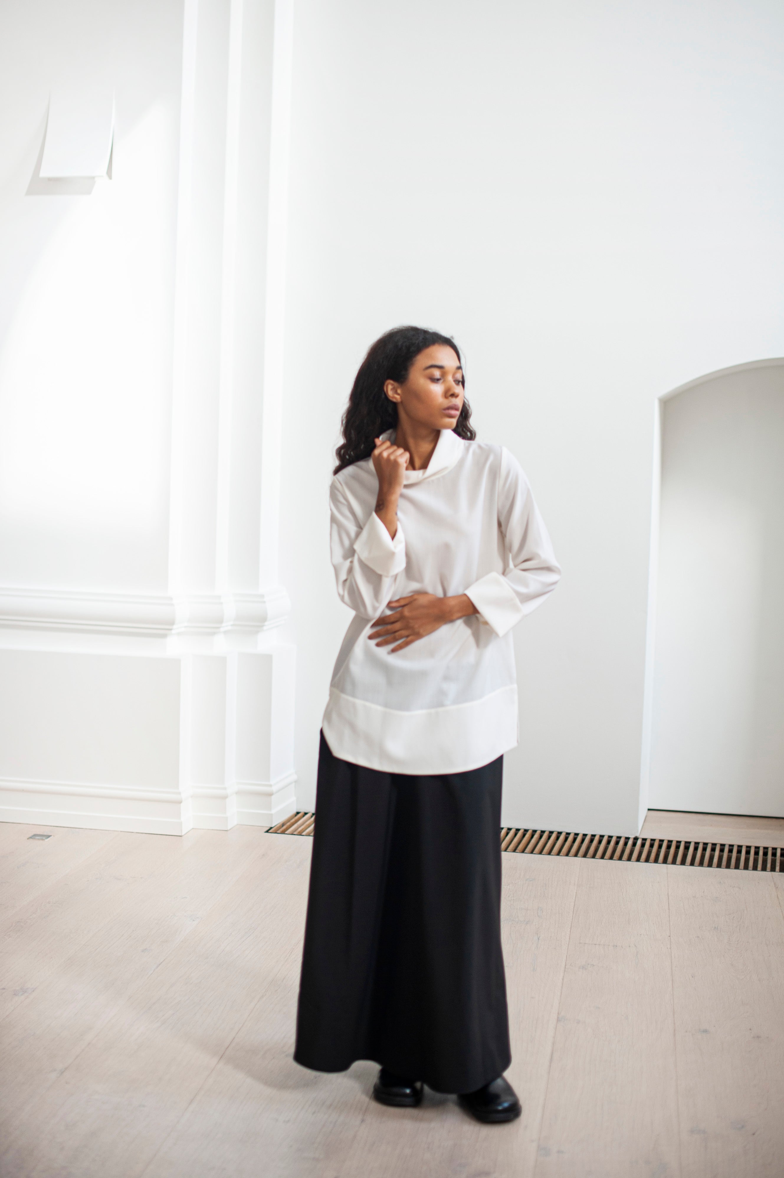 A duo of a white Merino wool blouse featuring a high neckline and wide cuffs. Paired with an elegant and feminine black wool skirt.