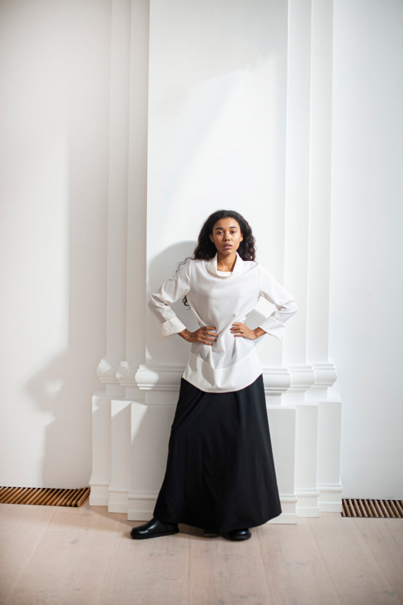 An ensemble of a black A-line skirt made of wool and a white blouse with a relaxed high neckline. Wide sleeve ends and hem for extra comfort.