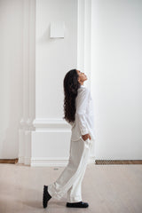 A white ensemble of a relaxed collared shirt in a fluid silhouette paired and  loose tapered trousers in a stripy pattern.